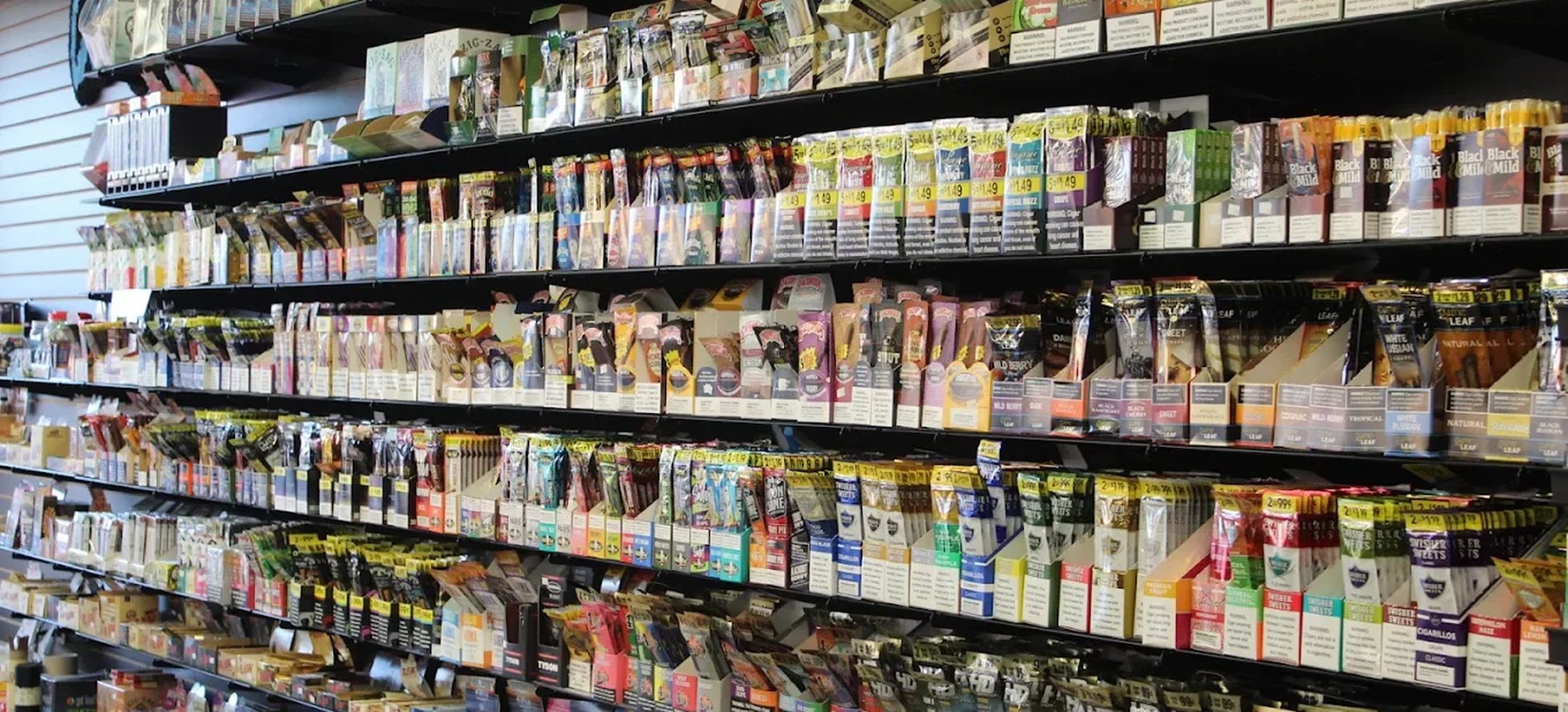 A wall of slatwall shelving at Infinity Smoke Shop stocked with rolling papers, wraps, cones, cigarillos and filtered cigars